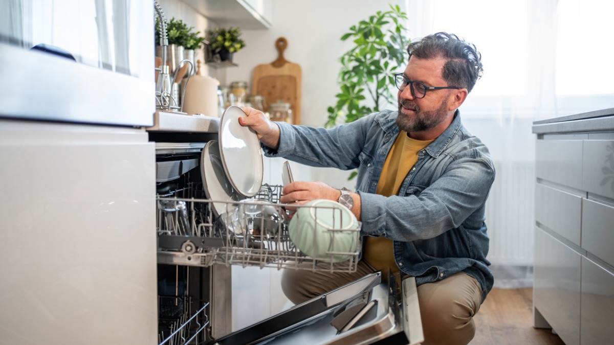 homme qui range son lave-vaisselle racordement eau chaude